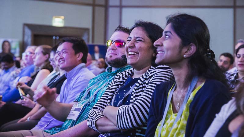 Smiling employees sitting in the audience during a keynote presentation